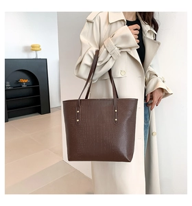 Detail of dark brown tote bag with crocodile pattern and gold rivet accents