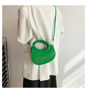 Model wearing emerald green pleated mini bag with circular handle and gold hardware