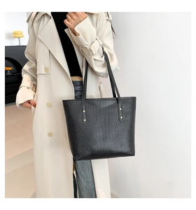 Detail showing crocodile-patterned black tote bag with gold stud hardware and shoulder straps