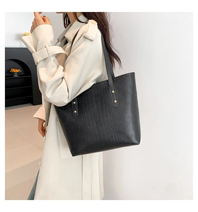 Detail of black crocodile embossed tote bag with gold rivets on beige trench coat
