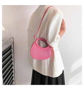 Detail view of pink semi-circular handbag with pleated leather texture and gold metal hardware