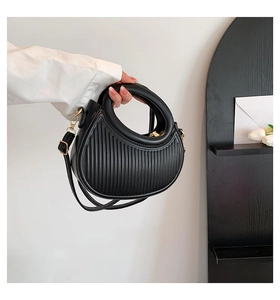 Detail of black pleated PU leather handbag with gold hardware and curved handle