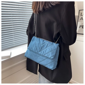 Détail du sac à bandoulière en denim bleu matelassé avec surpiqûres en V et chaîne dorée