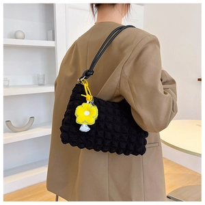 Detail of black puff textured shoulder bag with a yellow flower charm on a model