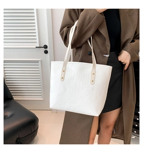 Detail shot of a white crocodile pattern tote bag featuring gold rivets and slim straps
