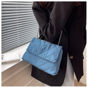 Détail d'un sac en jean bleu avec surpiqûres en V et bandoulière en métal doré