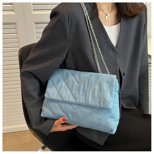 Détail du sac bandoulière en jean matelassé bleu clair avec chaîne dorée porté par un mannequin