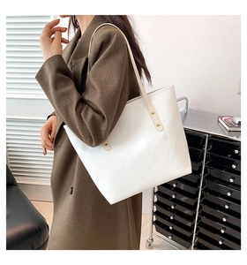 Detailed view of white crocodile pattern tote bag with gold rivets worn by a model