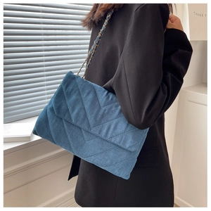 Détail du sac bandoulière en denim bleu matelassé chevron avec chaîne en métal doré