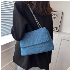 Détail du sac à bandoulière en denim bleu avec surpiqûres en V et chaîne en métal