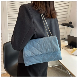 Détail du sac bandoulière en denim bleu clair avec matelassage en V et chaîne dorée