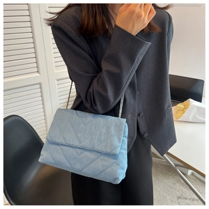 Détail du sac bandoulière en denim bleu clair avec matelassage en V et chaîne tressée