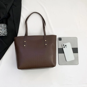 Detailed texture of dark brown crocodile pattern tote bag with shoulder straps and gold studs