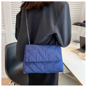 Détail d'un sac bandoulière en denim foncé avec matelassage en V et bandoulière chaîne
