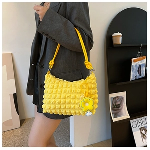 Close-up of bright yellow textured puff bag with thick rope strap and flower charm