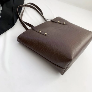 Detail of chocolate brown tote bag showing croc-effect texture and gold rivets
