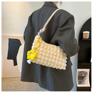 Detail view of cream puffer shoulder bag with rope strap and yellow flower charm