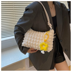 Detail of white waffle texture shoulder bag featuring a yellow flower charm and knot strap