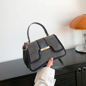 Elegante schwarze Lederhandtasche mit Strassklappe und goldener Schnalle auf dunklem Grund