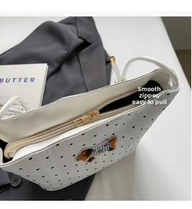 Detail of smooth golden zipper and bear embroidery on white polka dot lace bag