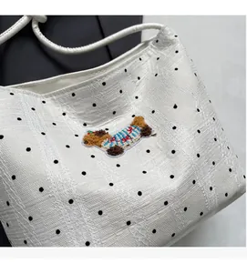 Close-up of white polka dot bucket bag featuring a detailed brown teddy dog embroidery