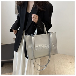 Detailed view of large silver tote bag with TOTE BAG relief and stylish leather straps