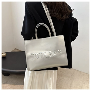 Macro shot of silver tote bag featuring textured TOTE BAG embossed design and metallic finish