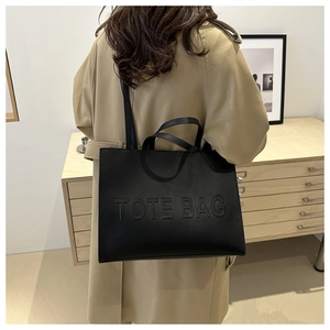 Detail of black tote bag with embossed lettering and smooth textured leather finish