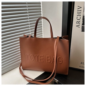 Detailed view of the embossed TOTE BAG text and fine leather texture on the brown tote