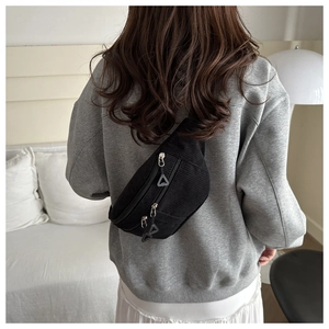 Close-up of black corduroy chest bag featuring unique triangle zipper pulls on a model