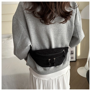 Detailed view of black corduroy waist bag with multiple zippers worn by model