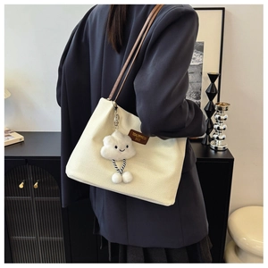 Detail of cream waffle texture tote bag with brown leather handles and a plush cloud charm