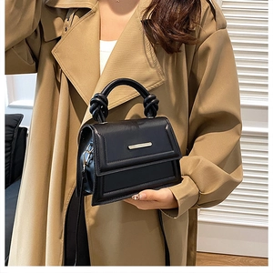 Detail of minimalist black crossbody bag with knot handle and metallic clasp on coat