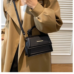Detailed view of black minimalist square crossbody bag with gold metal trim and strap