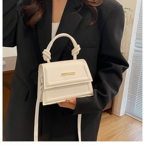 Detail of white leather handbag featuring a twisted top handle and gold metal bar