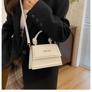 Close-up of white minimalist crossbody bag with knotted handle and gold metal detail