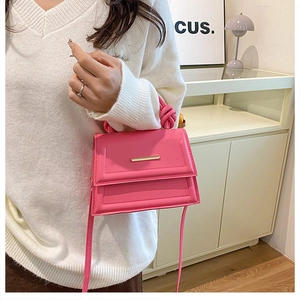 Close-up of pink square handbag featuring a knotted handle and sleek metal bar clasp