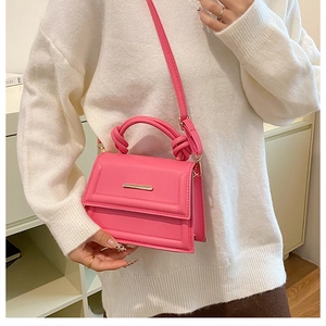 Detail of rose pink crossbody bag with knot handle and golden metal clasp on white sweater