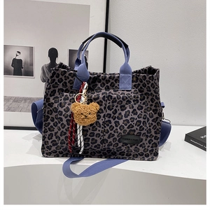 Detail of leopard print tote bag featuring blue straps and a plush bear pendant charm