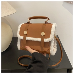 Detail of a brown leather crossbody bag with white faux fur trim and gold buckle