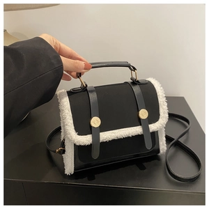 Close-up of black leather crossbody bag with white faux fur trim and gold metal buckles