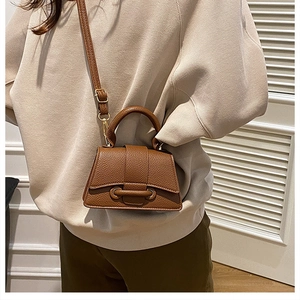 Detail of brown lychee leather handbag featuring a unique flap closure and top handle