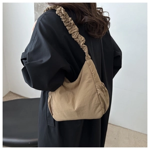 Close-up of khaki nylon tote with pleated shoulder strap on model in minimalist interior