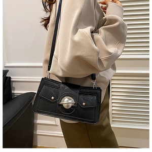 Détail d'un sac bandoulière noir avec grande boucle planète argentée et clous