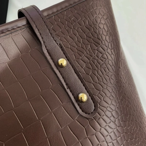 Detailed close-up of dark brown crocodile embossed leather with gold metal rivets