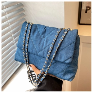 Détail du sac à bandoulière en jean bleu avec matelassage en V et bandoulière chaîne dorée