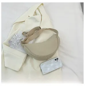 Detail view of a beige crescent moon crossbody bag with wide shoulder strap on fabric