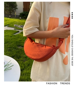 Close-up of orange nylon half-moon crossbody bag with adjustable strap on outdoor model