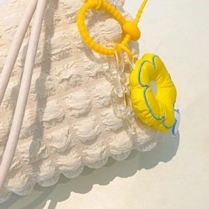 Detail of off-white waffle texture bag with bright yellow flower charm and acrylic chain