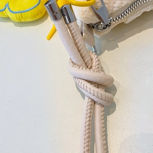 Close-up of knotted leather strap and silver zipper on soft plush beige handbag